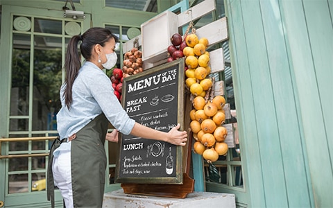 Image of woman, wearing a mask, who is putting a sign outside of her shop