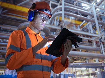 Man in jumpsuit with pipes behind him with tablet