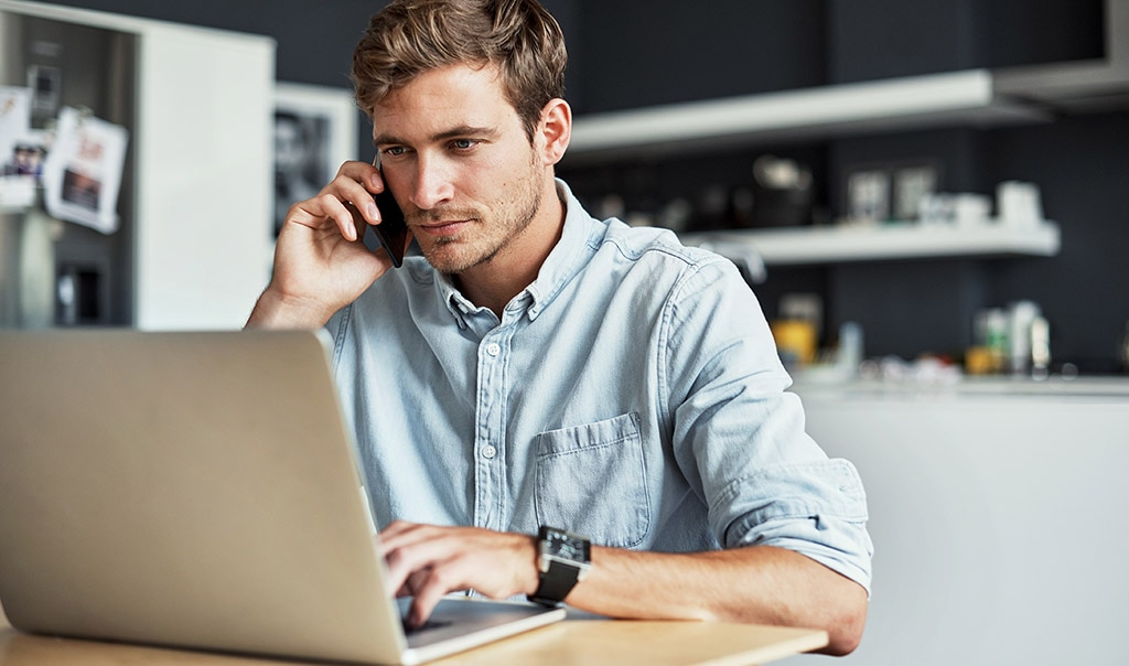 man wearing blue shirt, on laptop and cell phone