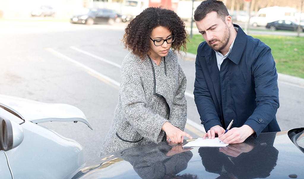 female and male writing on paper  - hood of car