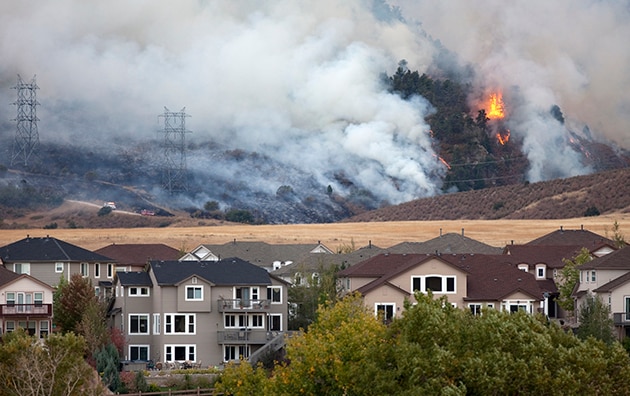 A wildfire burning in the background near a neighborhood in the foreground.